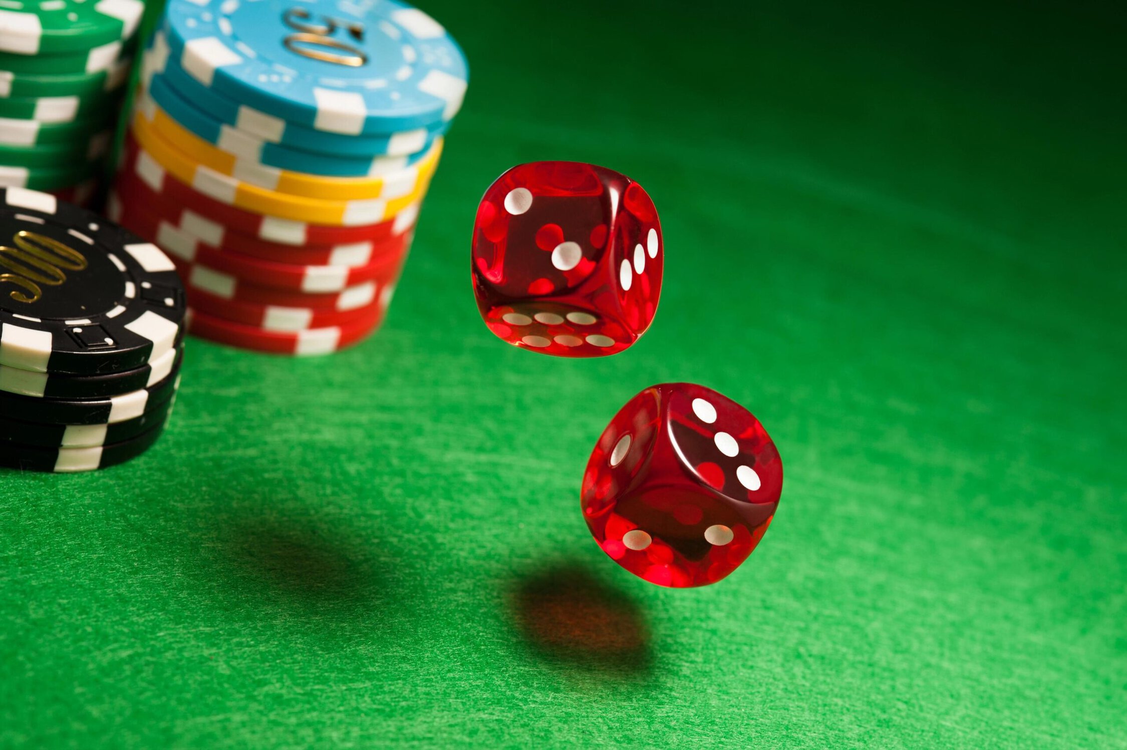 Two red dice and poker chips on a green felt table for gambling or casino games.