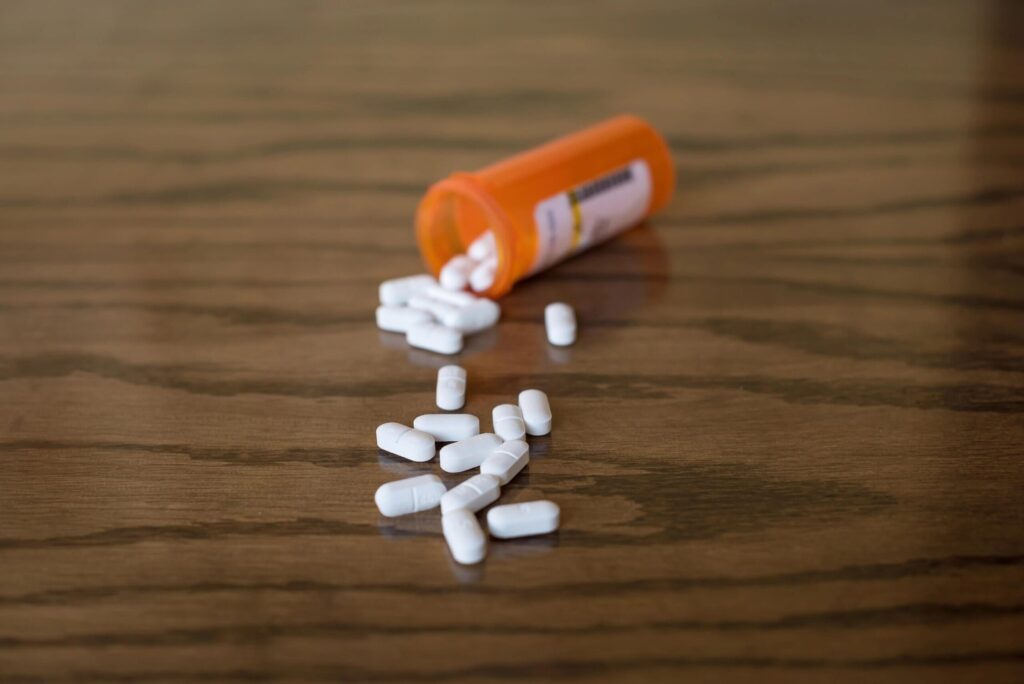 Opiate pills spilled from prescription bottle on wooden surface.
