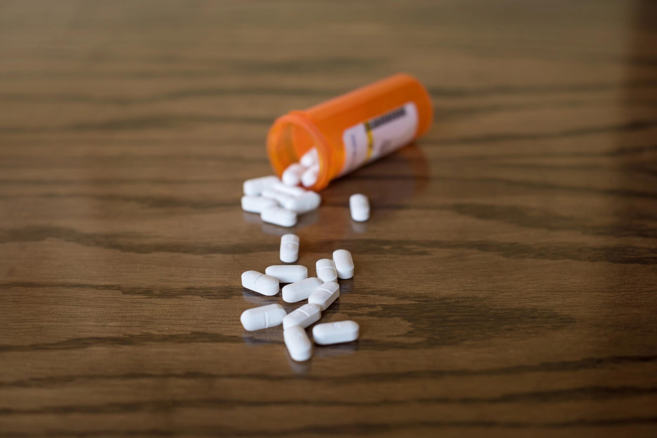 Opiate pills spilled from prescription bottle on wooden surface.
