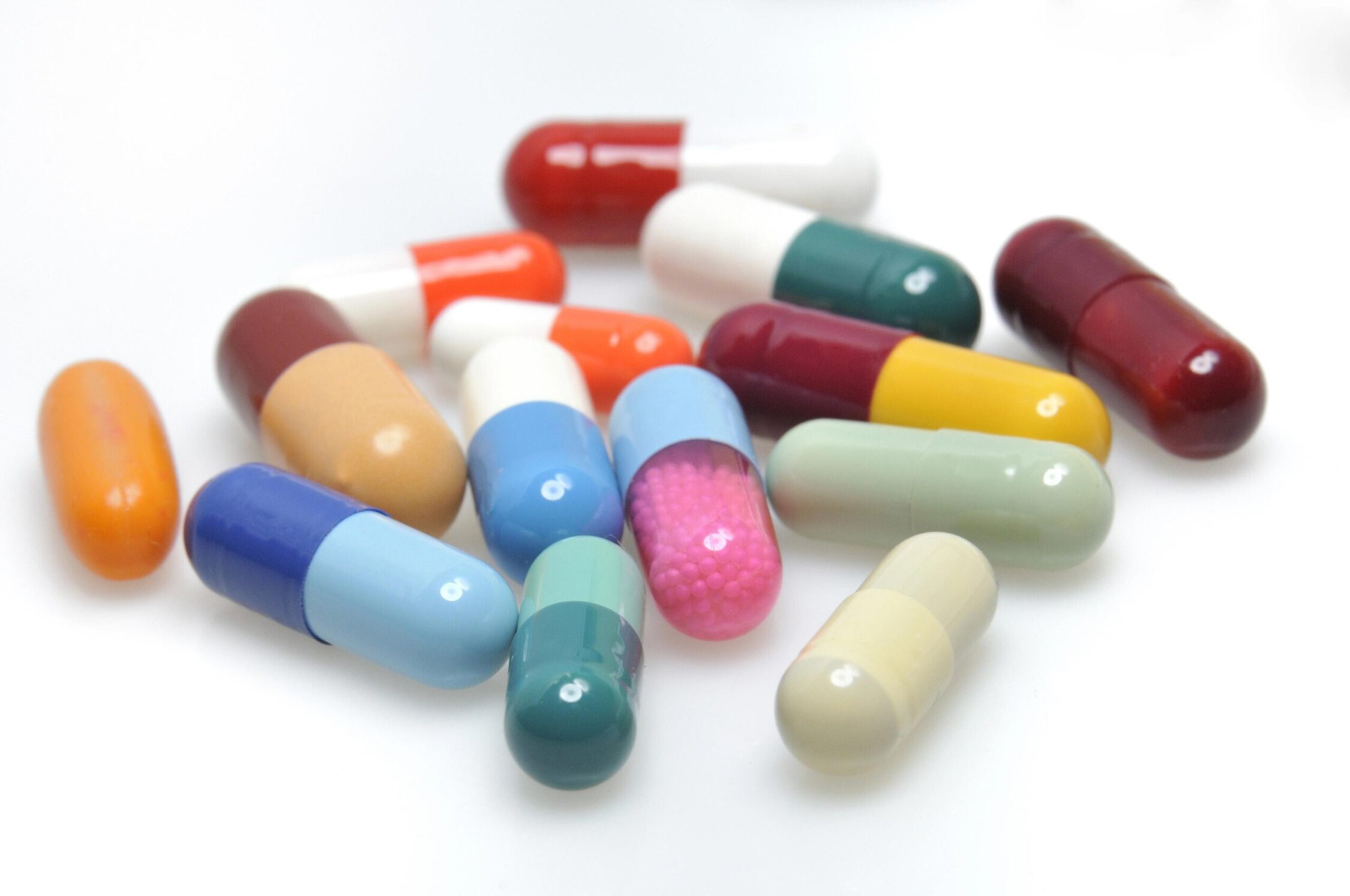 Pills and capsules in various colors and shapes scattered on a white background.