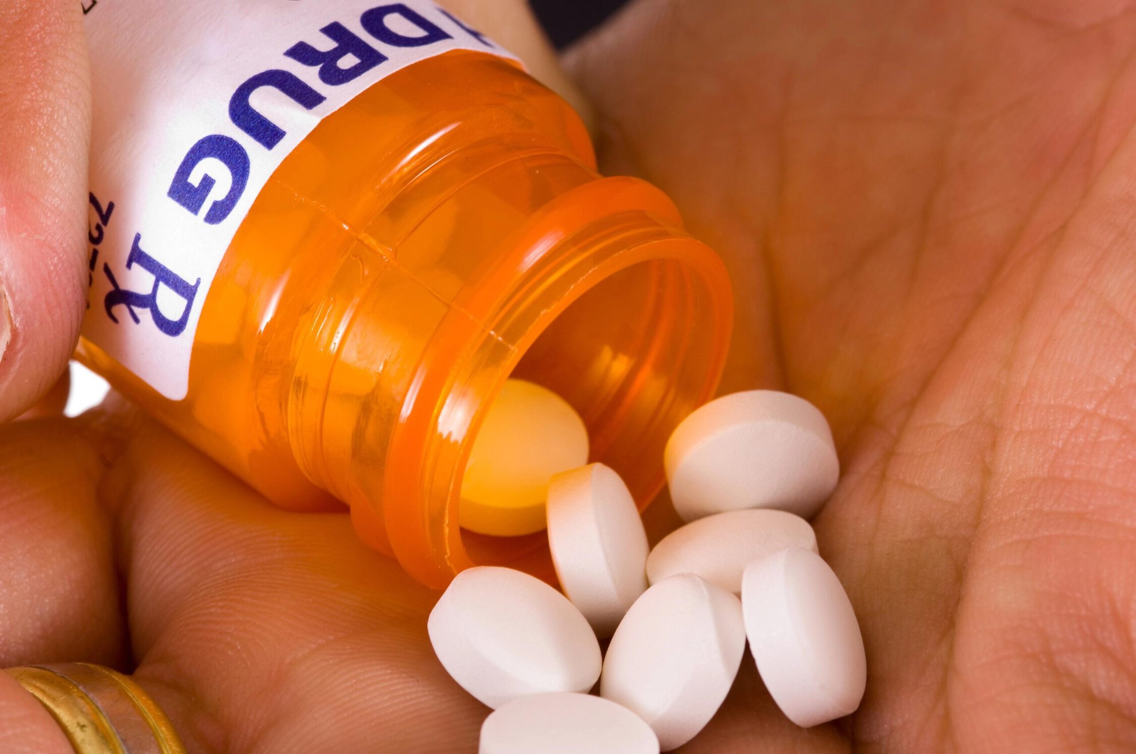 Pill bottle spilling white tablets into hand.