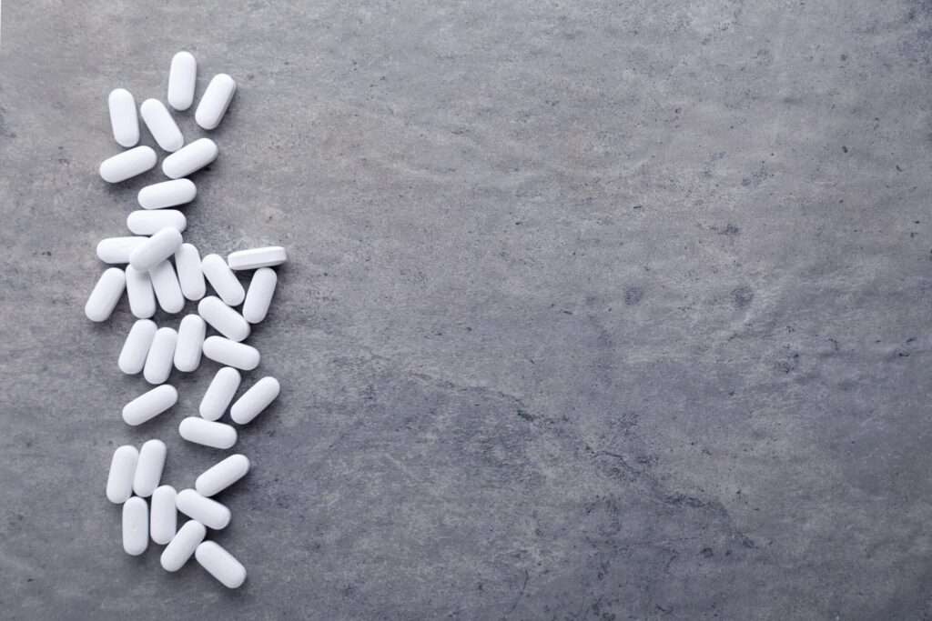 White pills scattered on a gray surface, symbolizing medication or substance use.