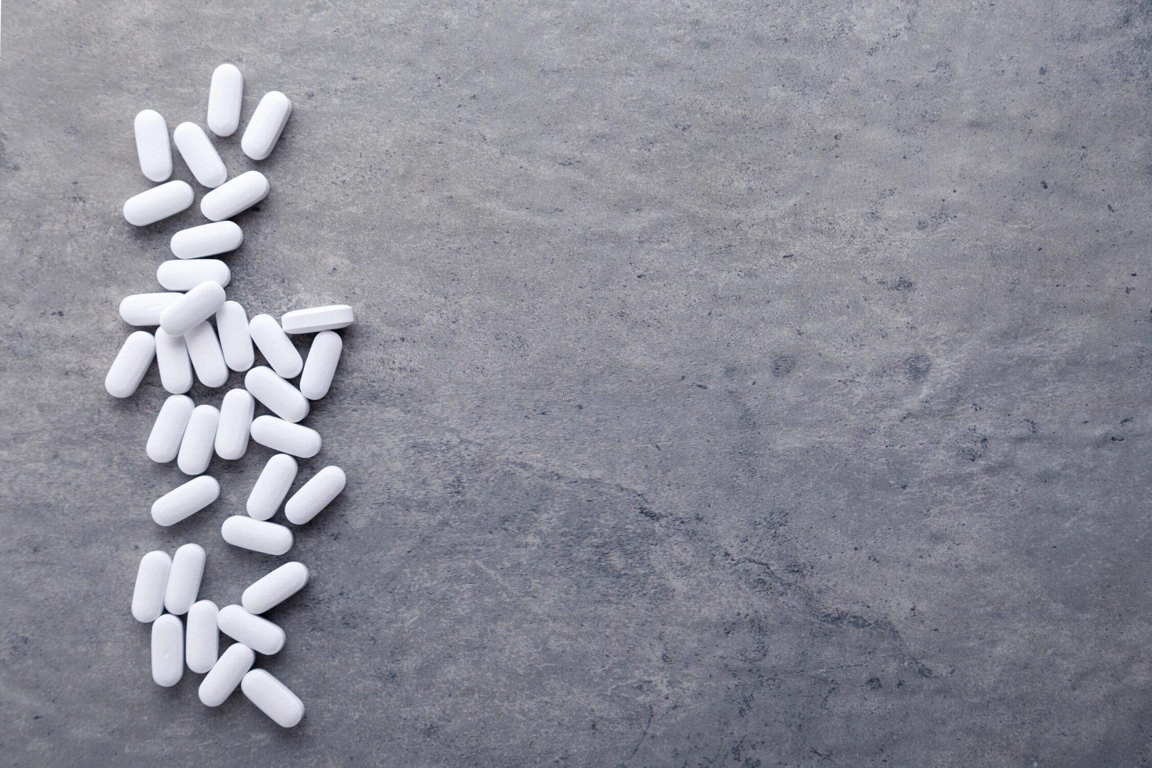 White pills scattered on a gray surface, symbolizing medication or substance use.